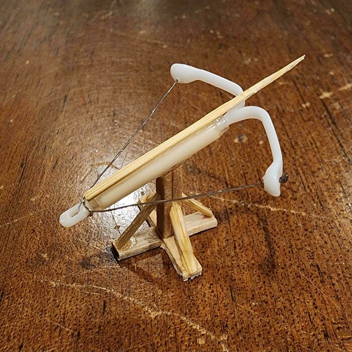 A miniature handmade crossbow crafted from wood and white plastic, sitting on a wooden surface. Handmade projects that took talent.