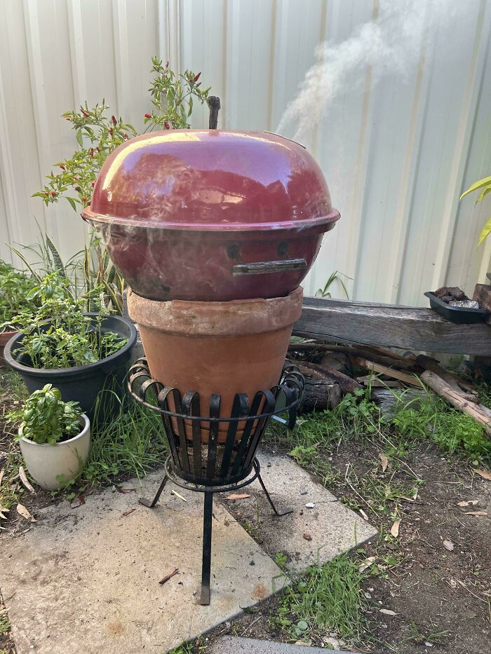 A red dome barbecue grill set atop a terracotta pot on a stand, a clever solution for outdoor cooking.