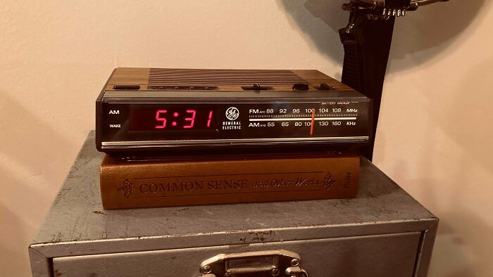 A retro General Electric alarm clock, displaying 5:31, sits on a book atop a metal cabinet. A nostalgic look into older times.