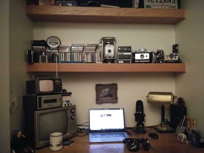 A desk with retro pics, including vintage cameras, old TVs, cassette tapes, and a modern laptop.
