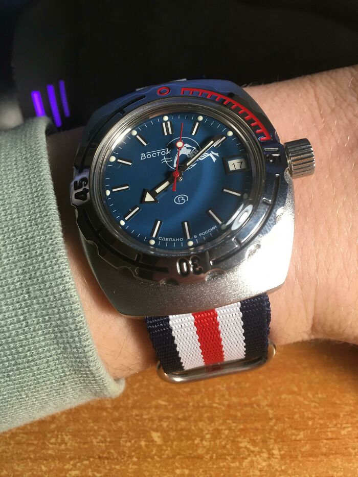 A retro pics Vostok Amphibia watch on a wrist with a blue, red, and white striped nato strap, showing a blue dial.