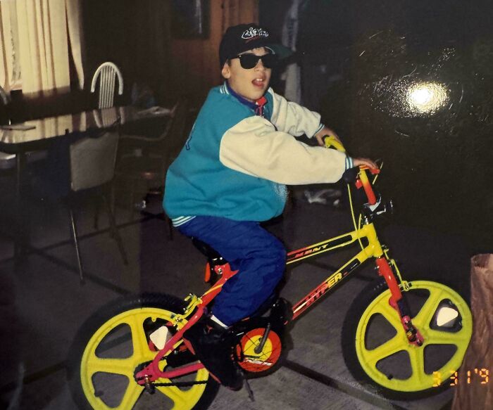 A young boy in a backward baseball cap and sunglasses on a vibrant yellow and red retro BMX bike, a cool pic from older times.