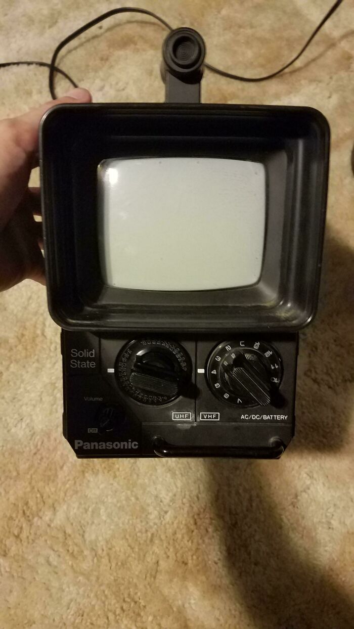 A person holding a small, black retro Panasonic Solid State TV on a light brown carpet. It's a true time machine into older times.