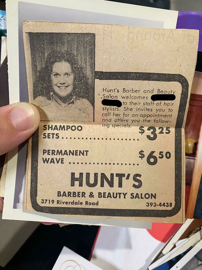 A person holding a retro newspaper ad for Hunt's Barber & Beauty Salon with a photo of a smiling woman, showcasing older times.