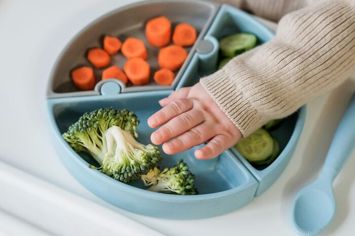 Child's hand reaching for broccoli from divided plate with random facts