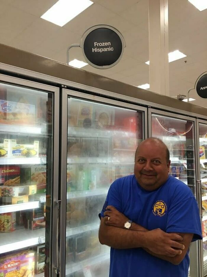 A smiling man with crossed arms in a blue shirt next to a freezer labeled Frozen Hispanic. Blessed images of positivity.