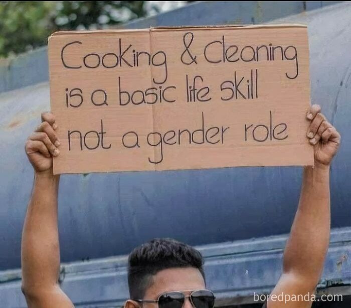 A person holding a cardboard sign that says 'Cooking & Cleaning is a basic life skill not a gender role', spreading positivity.