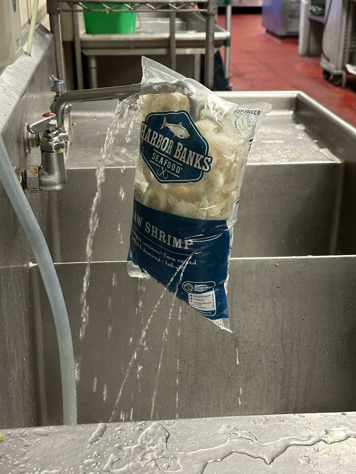 Bag of frozen shrimp hanging over dirty kitchen sink with leaking water