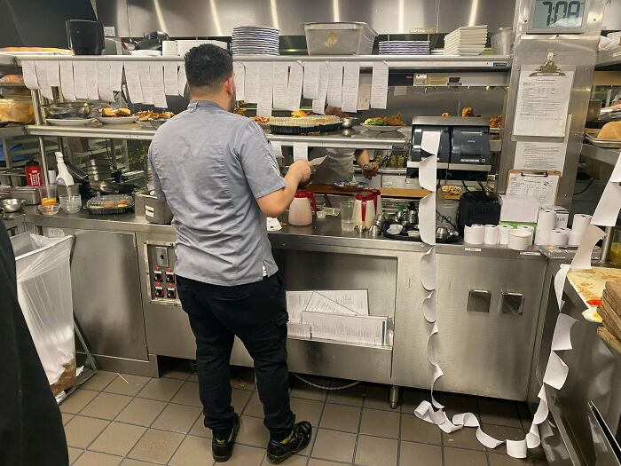 Busy restaurant kitchen with worker handling orders and printed tickets