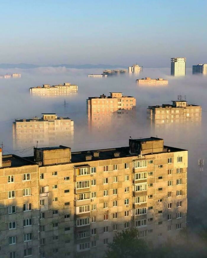 Urban hell buildings emerging from dense fog in cityscape