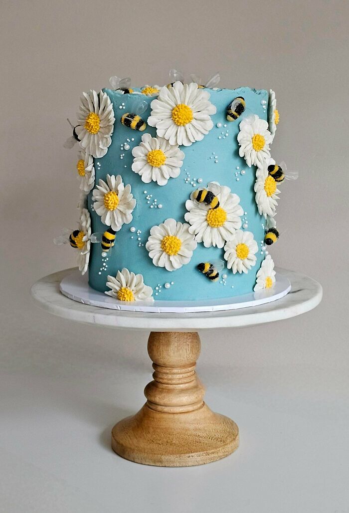 Blue cake decorated with white daisies and edible bees