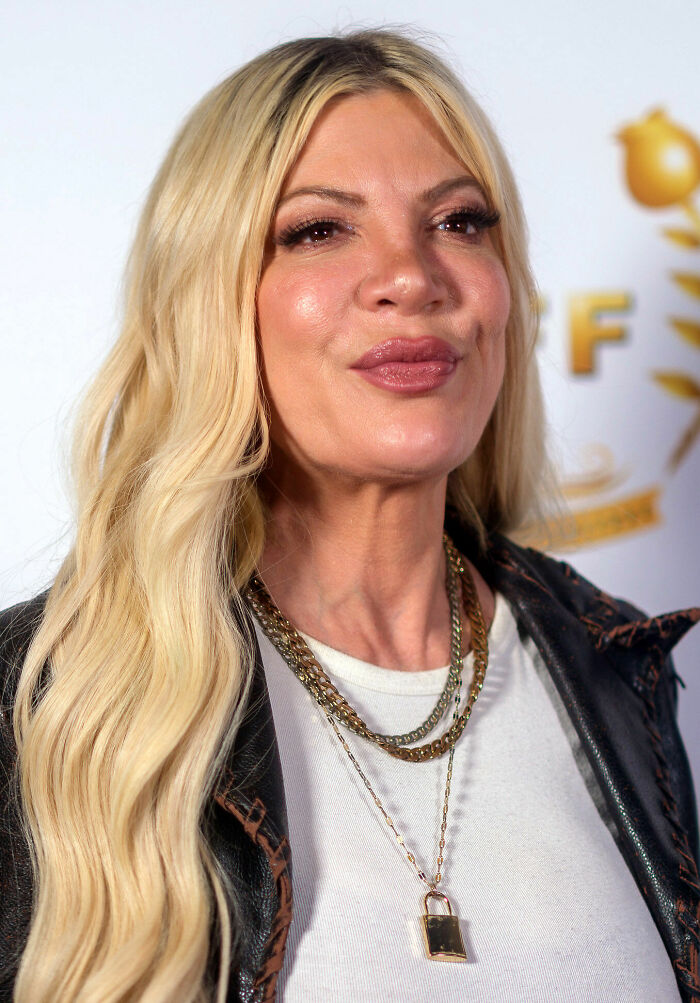 Close-up portrait of Tori Spelling with long blonde hair and layered gold necklaces