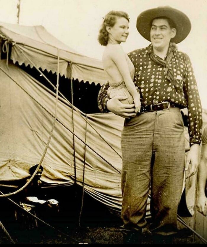 Historical photo of a giant man holding a tiny woman near a tent, offering an interesting and uplifting post.