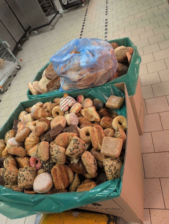 Two large bins overflowing with various types of bread and pastries, demonstrating excessive consumerism and food waste.