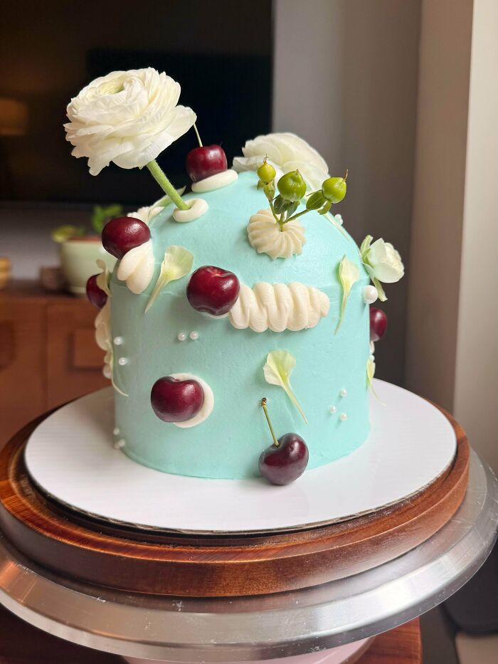 Blue cake adorned with cherries, white flowers, and green berries