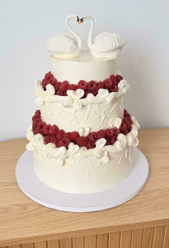 Elegant white cake decorated with raspberries and swan cake toppers