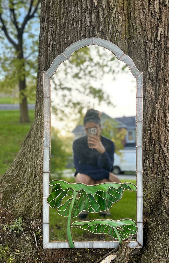A beautiful handmade mirror with an arched top and stained glass lily pads, reflecting a person and a tree. Handmade projects that took talent.
