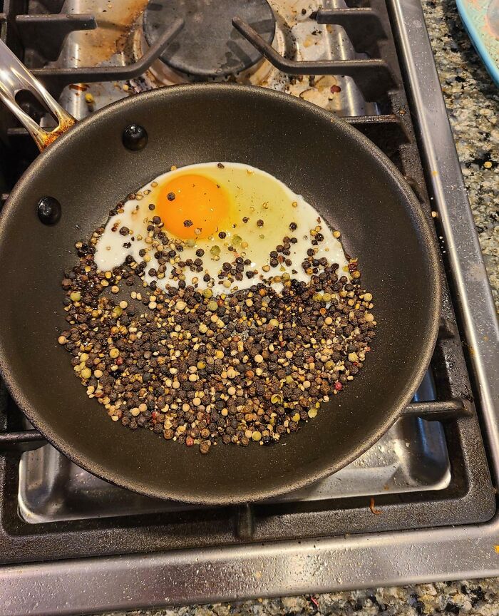 Kitchen fail with egg cooking in pan full of black peppercorns