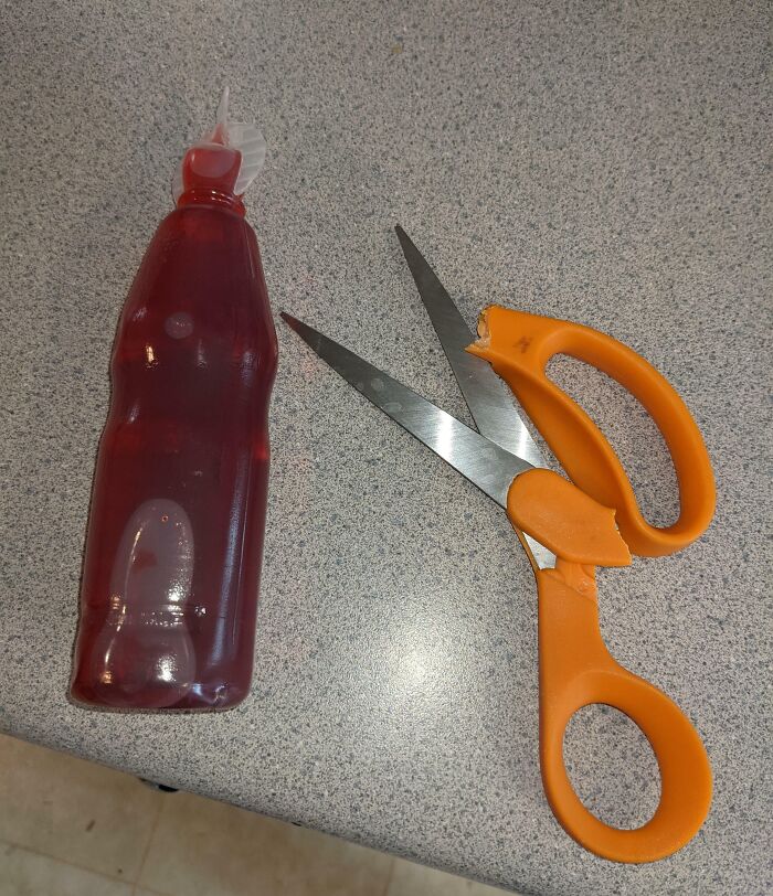 Kitchen scissors with broken handle next to red condiment bottle on countertop