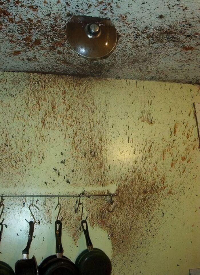 Kitchen wall and ceiling heavily stained with grease and grime around hanging pans