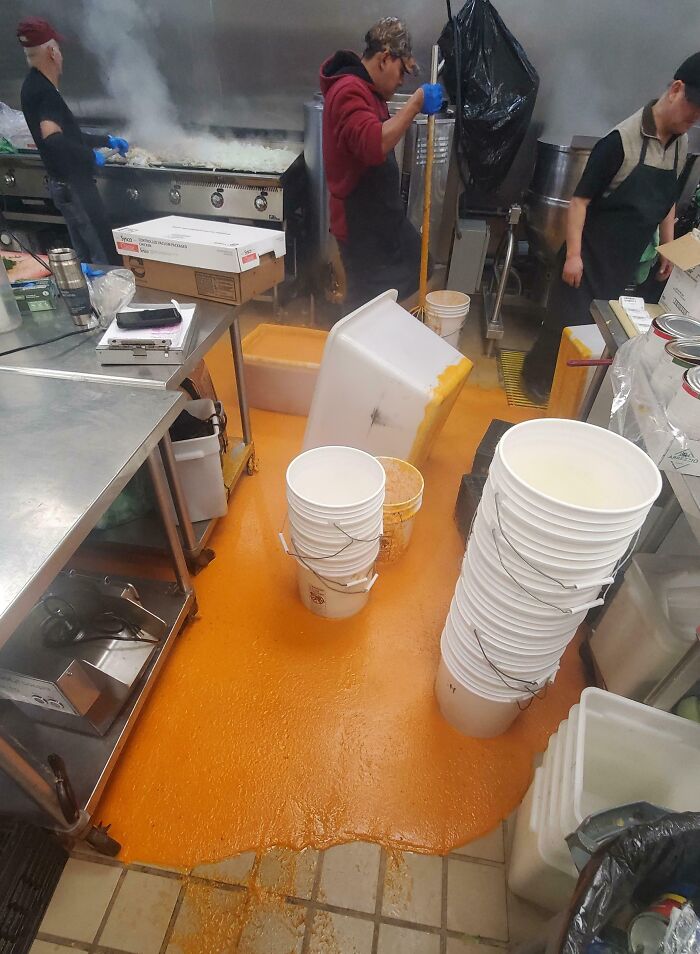 Bright orange sauce spilled across restaurant kitchen floor with workers cleaning up kitchen fail