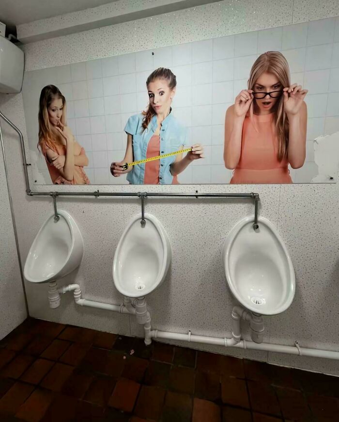 Bathroom urinals below poster of women measuring waist with tape, humorous juxtaposition