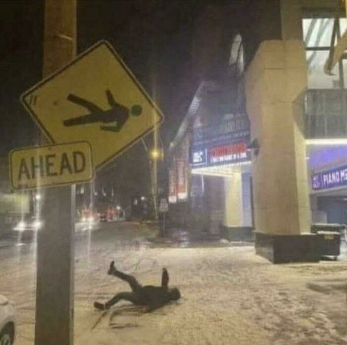 Funny street sign showing person falling ahead matching person lying on snowy street