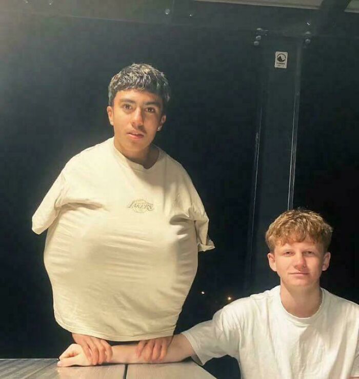 A humorous photo of two men with one man wearing an oversized shirt making his head appear small