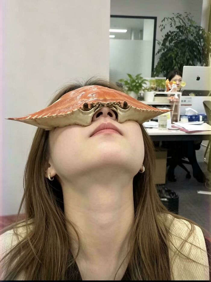 Woman wearing a crab shell on her face in an office setting