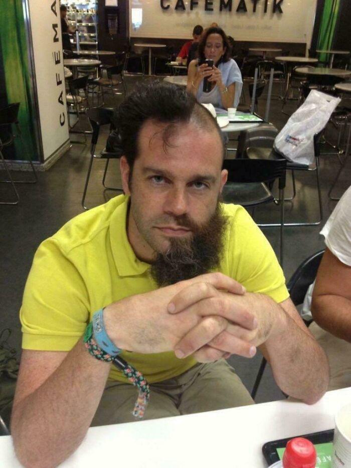 Man with half-shaved head and half-shaved beard sitting in cafe