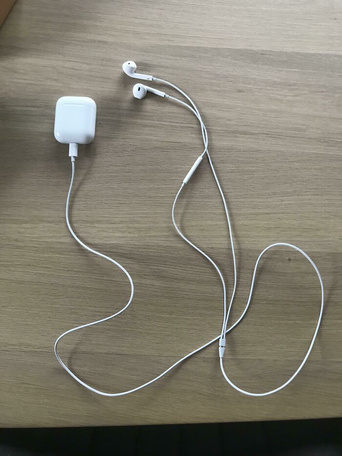 White wired earbuds with tangled cable on wooden surface