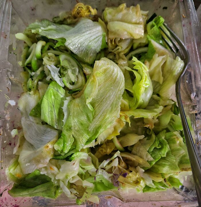 Partially eaten salad in plastic container with fork