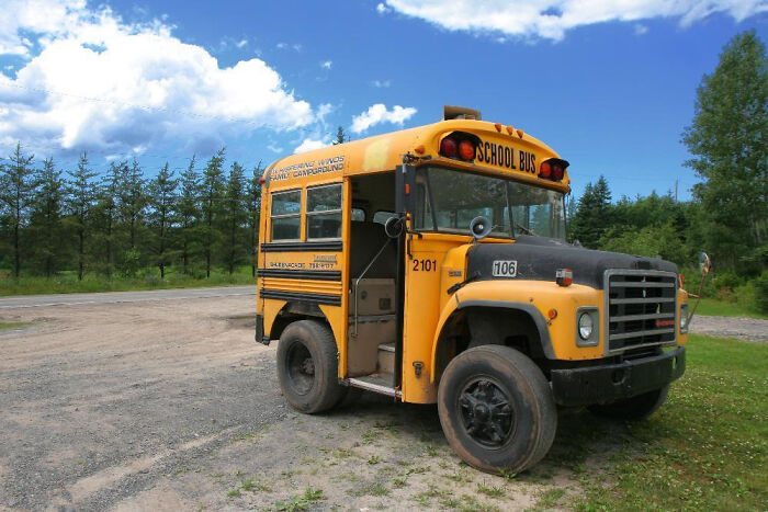 Old yellow school bus parked on gravel under blue sky