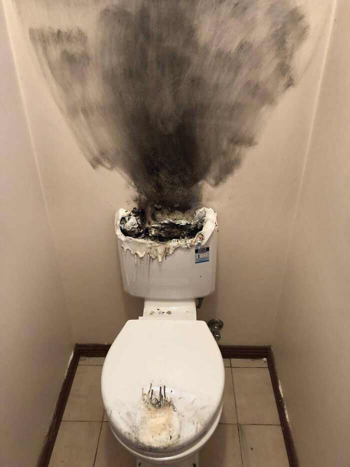 Burned toilet with melted tank and black soot on wall in bathroom fire damage