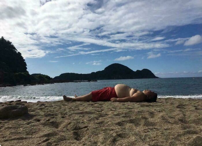 Man lying on beach with belly blending into sand in funny perspective