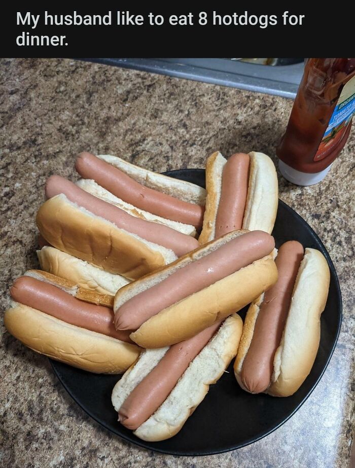Plate piled with eight plain hotdog buns and hotdogs on kitchen counter