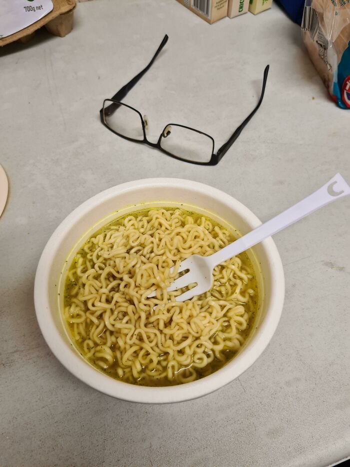 Absurd moment with cooked instant noodles in bowl and glasses on table