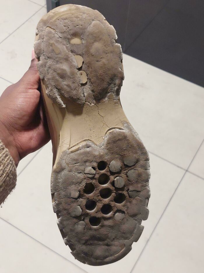 A hand holding up a shoe with a heavily worn and damaged sole, illustrating insulting consumerism and poor quality.