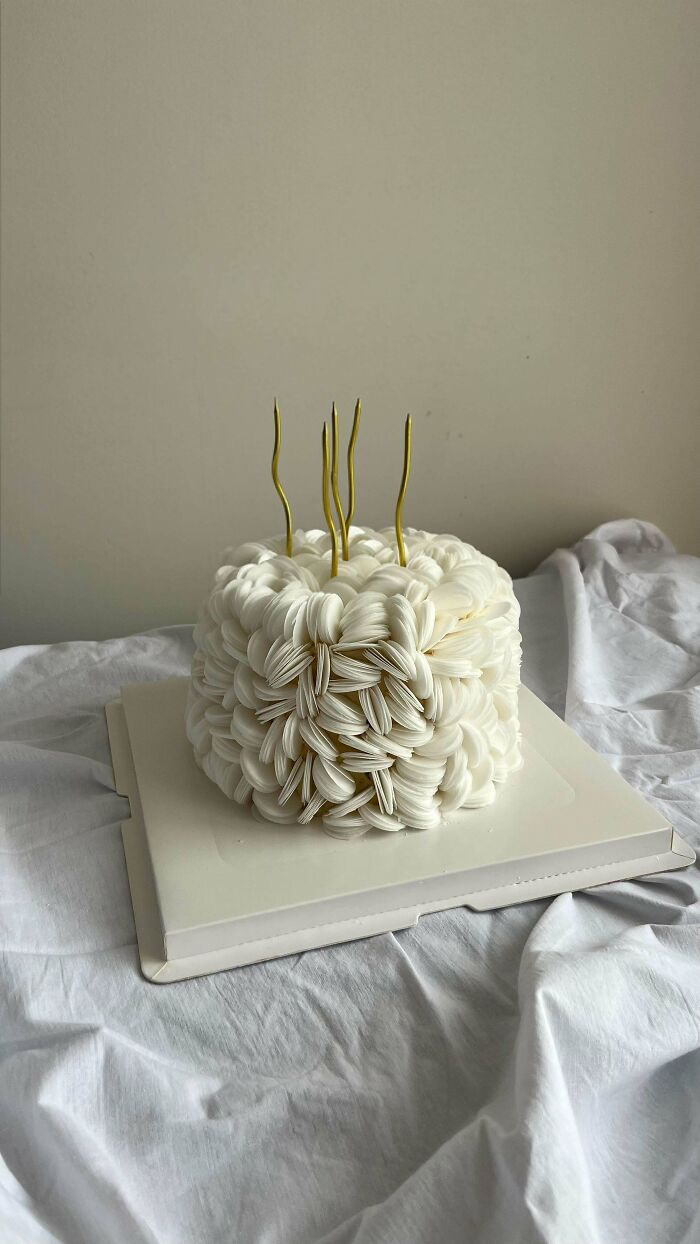 White textured birthday cake with gold candles on a white cloth background