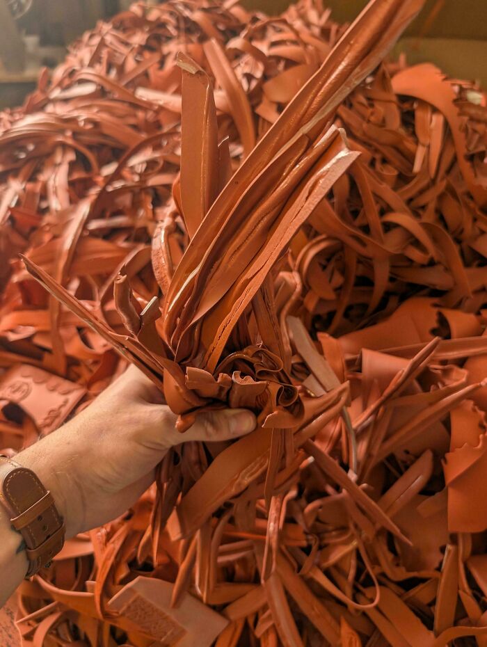 A hand holding a bunch of leather scraps, representing waste in consumerism.