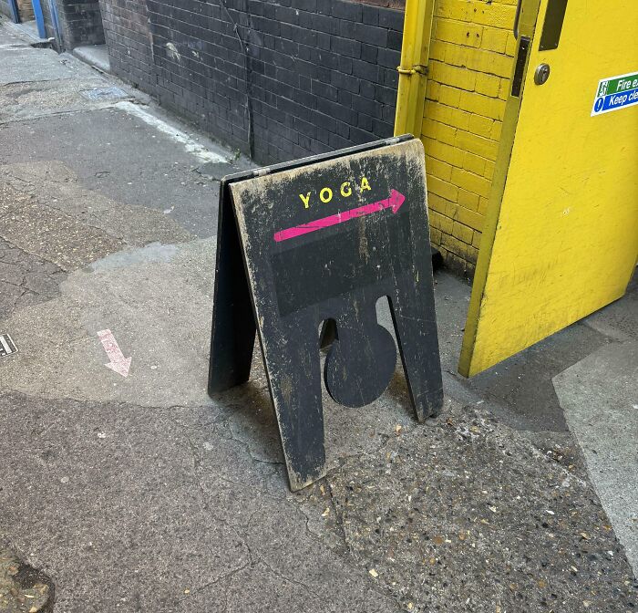 Black sandwich board with yoga direction arrow on a worn street near yellow door