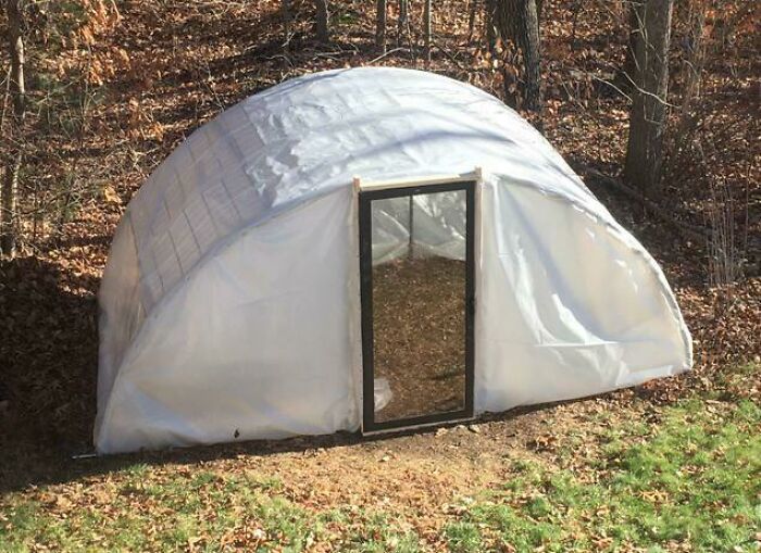 Homemade greenhouse built with plastic sheeting and wooden frame in yard
