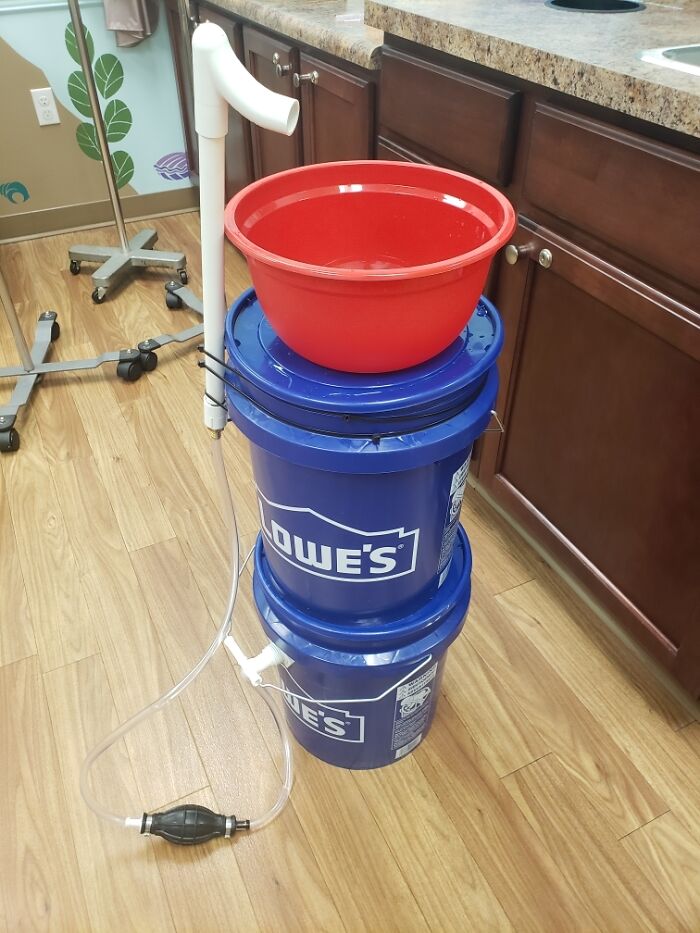 DIY handwashing station using stacked buckets, basin, and pipe indoors