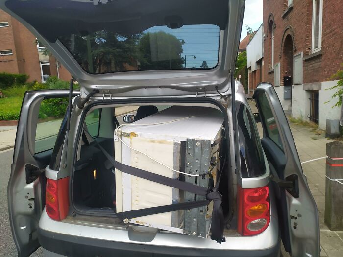Carrying large item in hatchback car secured with seat belts low-tech method