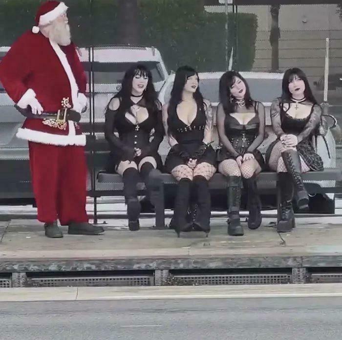 Santa standing next to four women dressed in gothic black clothing