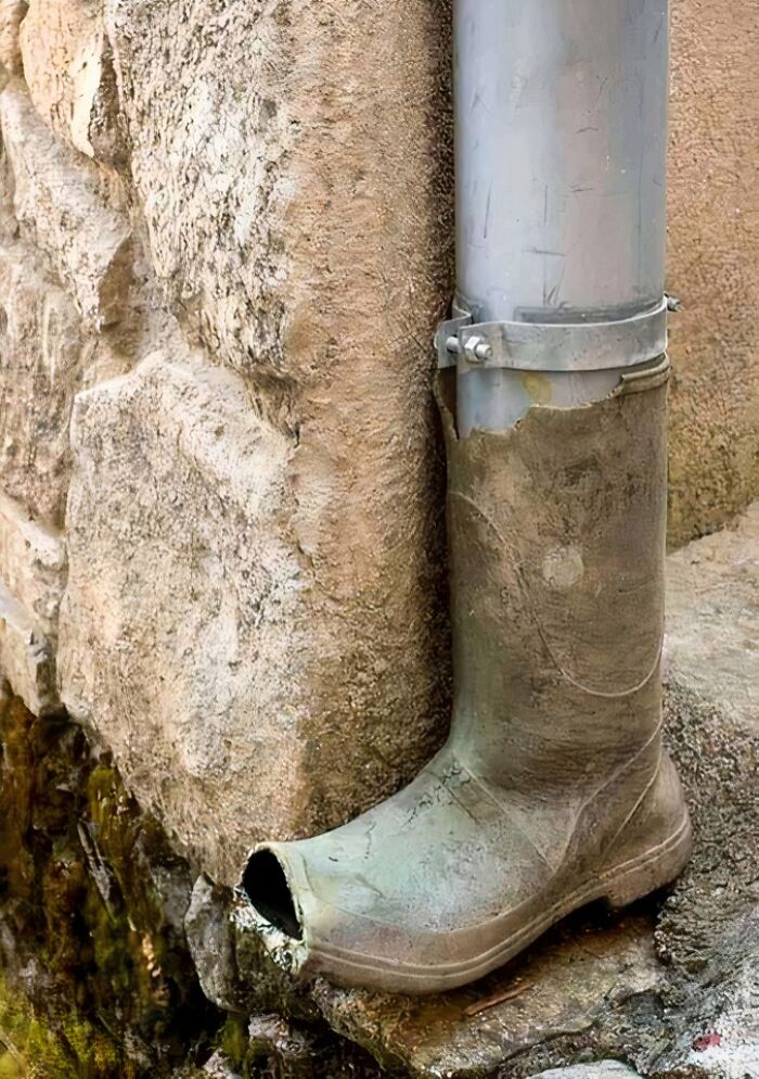 Old boot repurposed as a low-tech drainage pipe cover on exterior wall