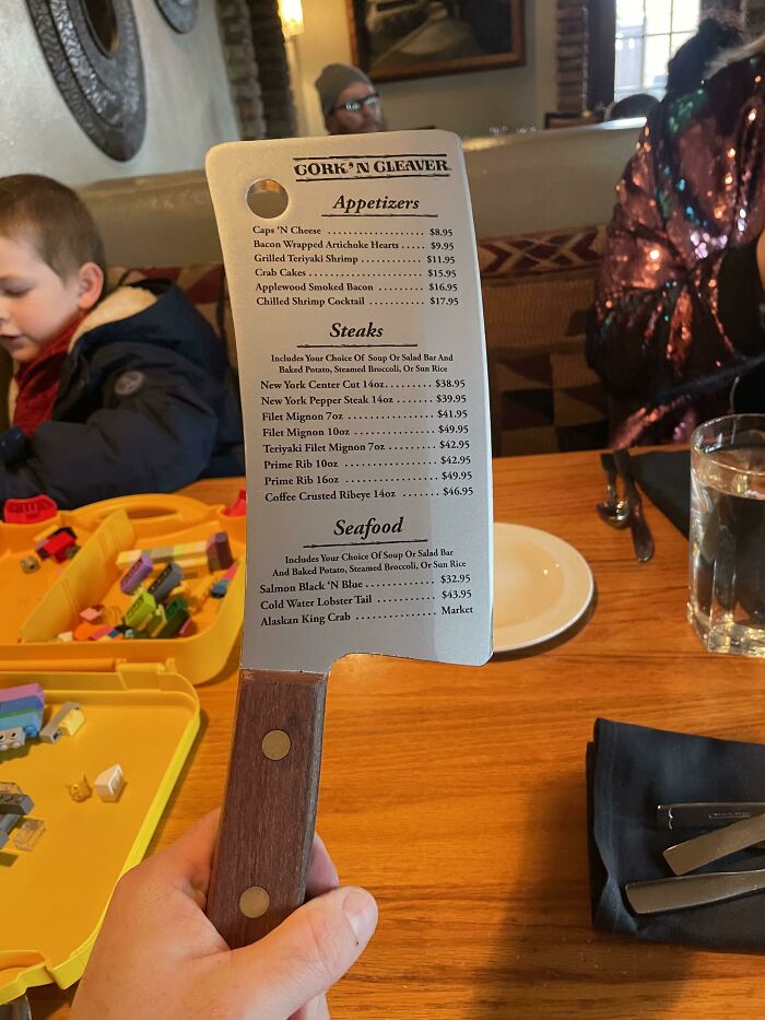 Restaurant menu printed on a cleaver-shaped board held by a person