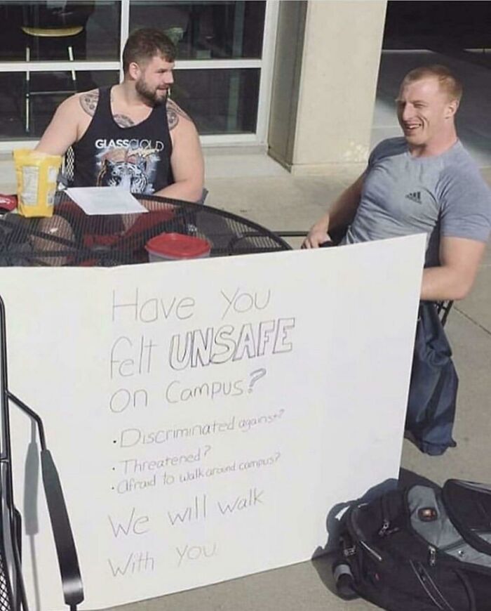 Two men seated outside with a sign offering campus safety walks
