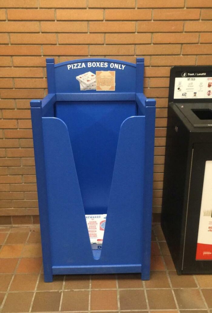 Blue recycling bin for pizza boxes placed next to trash can in school hallway