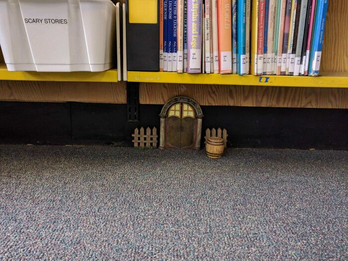 Miniature fairy door and fence under a library bookshelf
